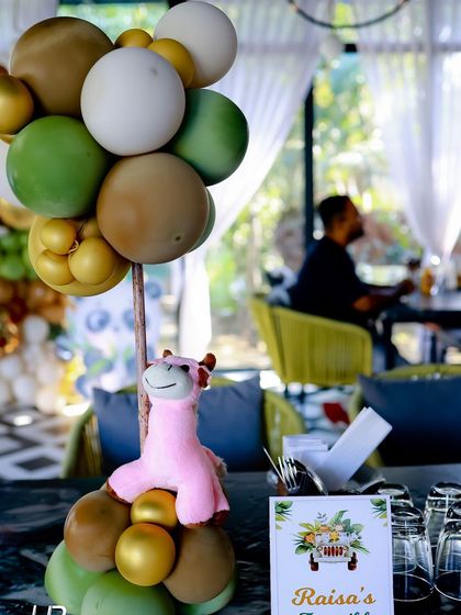 A close up of a table centerpiece from the "Two Wild" party, featuring a balloon cluster in safari colors and a cute pink giraffe plush toy.
