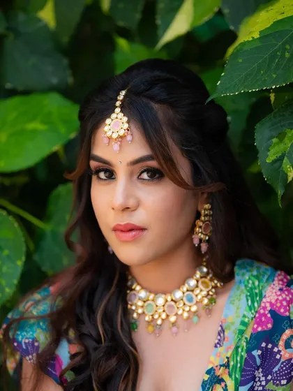 A close-up portrait of a model's Mehendi look. The focus is on her expressive eyes and the colorful makeup and jewelry, perfect for festive occasions.