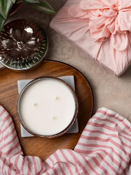 This intricately crafted silver container holds a three-wick candle, perfect for creating a beautiful ambiance. The gift is wrapped in pink Furoshiki cloth.