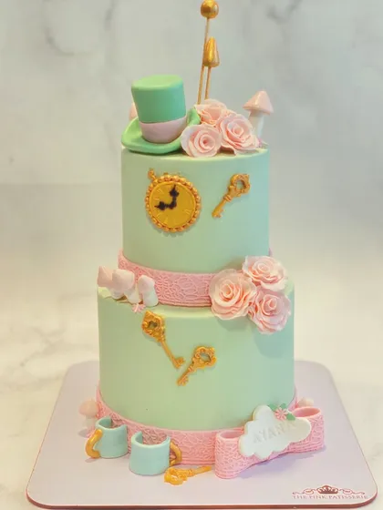An "Alice in Wonderland" inspired two-tiered cake. This whimsical design features the Mad Hatter's hat, clocks, keys, and roses in a soft pastel palette.