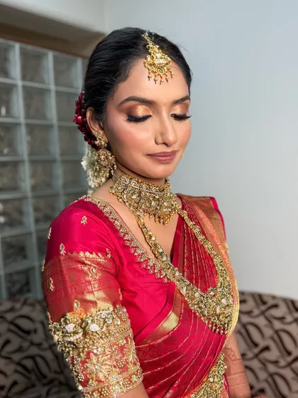A close-up of a South Indian bridal look. The makeup features a golden-bronze eyeshadow, winged liner, and a soft matte lip, perfectly complementing the traditional gold jewelry.