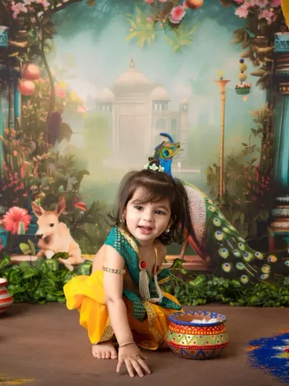 A delightful photo of a young child as Krishna, holding flowers with a bright smile, set against the detailed and colorful Vrindavan-inspired scene.
