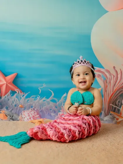A wide-eyed, joyful expression from our little mermaid. The pastel-colored coral and balloon backdrop creates a soft, dreamy atmosphere for the photoshoot.