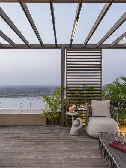 This duplex terrace in Surat offers an oasis of contemporary calm with expansive views of the Tapi River. We designed this outdoor space as a seamless extension of the interior, using a wooden pergola and minimalist furniture to create a sophisticated area for relaxation and entertainment, blurring the lines between inside and out.
