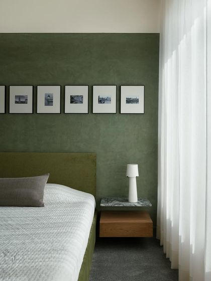 Another angle of the master bedroom, showing the low-profile green bed and the custom floating nightstand. The design prioritizes visual softness and a connection to the natural light.