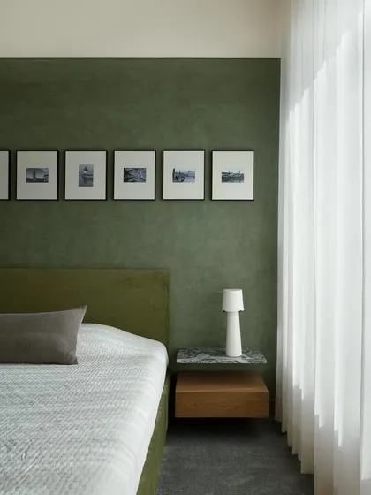 Another angle of the master bedroom, showing the low-profile green bed and the custom floating nightstand. The design prioritizes visual softness and a connection to the natural light.