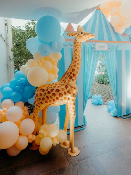 A life-sized giraffe prop adds a "wow" factor to this carnival-themed party entrance, complemented by a blue and yellow balloon arrangement.