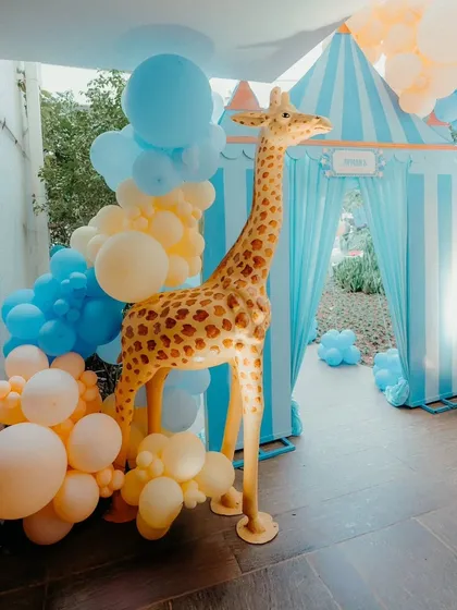 A life-sized giraffe prop adds a "wow" factor to this carnival-themed party entrance, complemented by a blue and yellow balloon arrangement.