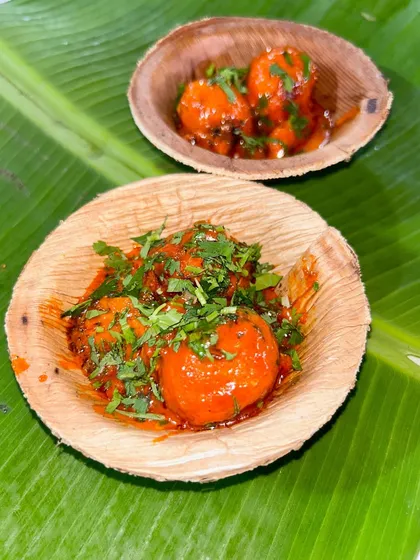 My Hot Sizzling Bonda, served in eco friendly leaf bowls. The bondas are coated in a rich, spicy sauce and garnished with fresh cilantro, ready to be enjoyed by guests.