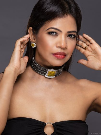 A portrait of a model wearing a statement choker, with her hands framing her face.