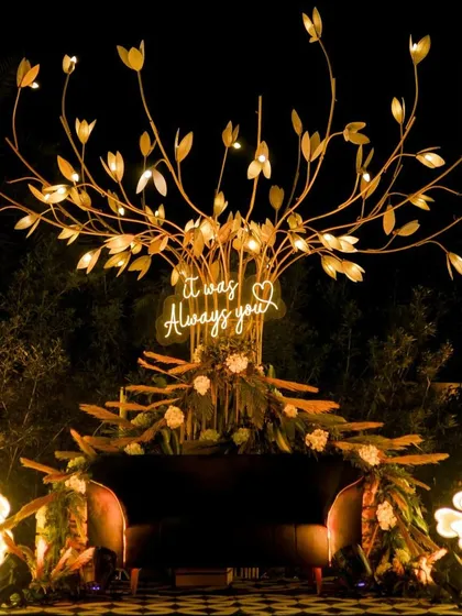 A romantic photo booth with a lit-up tree and a neon sign saying "It was Always you," perfect for couple photos.