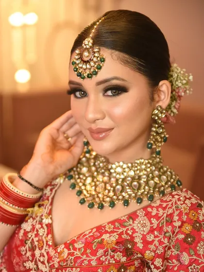 A beautiful portrait of a bride in a classic red lehenga, adorned with a heavy Kundan necklace set that perfectly complements her smoky eye makeup.
