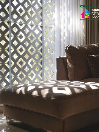 Light filtering through the Rangoli-inspired jaali screen casts intricate shadows on the sofa. This is how we use architecture to create moments of beauty in everyday life.