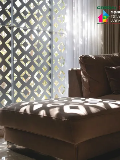 Inside, the 'jaali' screen filters the harsh sunlight, casting intricate geometric shadows across the living room and furniture, creating a dynamic and ever-changing ambiance.