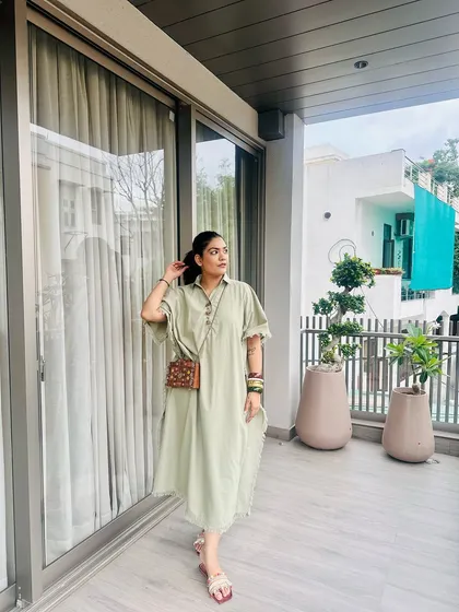 This pose highlights the delicate chain strap of the wooden clutch, allowing it to be worn as a shoulder bag for added convenience.