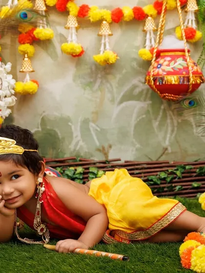 A playful little Krishna lies on the grass, looking coyly at the camera during his photoshoot.