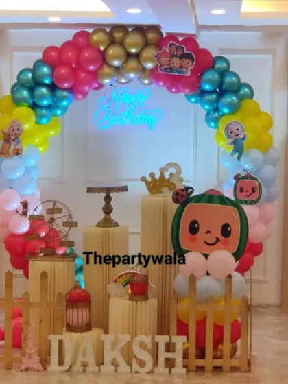 A Cocomelon theme with a neon "Happy Birthday" sign and a colorful balloon arch. The watermelon balloon sculpture is a fun and unique detail.