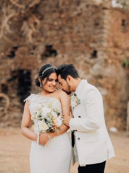 An intimate portrait with the groom gently kissing the bride's shoulder. The rustic stone wall provides a timeless and textured background for this romantic shot.