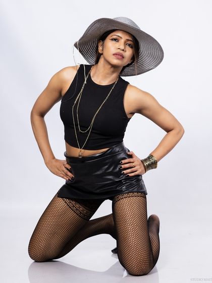 A model in a black crop top, leather skirt, and a wide-brimmed hat, in a kneeling pose.
