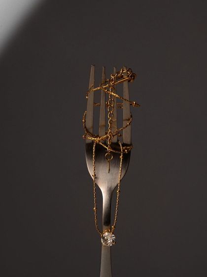 An unconventional shot of gold jewelry wrapped around a fork. This artistic and unexpected pairing creates a highly memorable image.