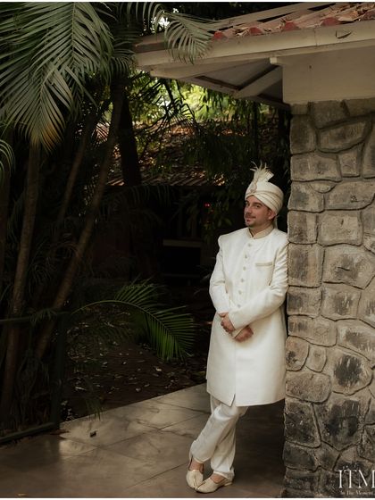 A full-length portrait of the groom leaning against a stone wall. His relaxed yet elegant pose captures a moment of quiet confidence before the ceremony.
