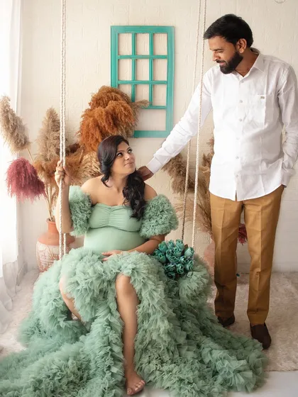 A dreamy maternity portrait on a studio swing. The flowing green dress and boho setup create a whimsical and romantic scene.