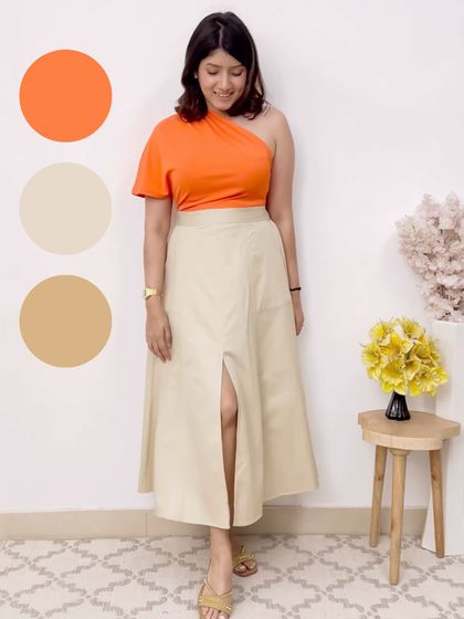 This outfit combines a bright orange one-shoulder top with a neutral beige skirt. The pop of color is balanced by the muted tones of the skirt, creating a fun yet grounded look.