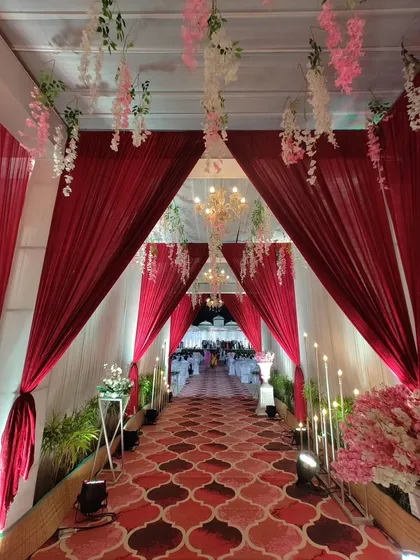 A classic and elegant entrance is always a beautiful choice. Here, I used rich red and white drapes to create a long, inviting walkway, illuminated by warm candlelight and delicate hanging floral arrangements.