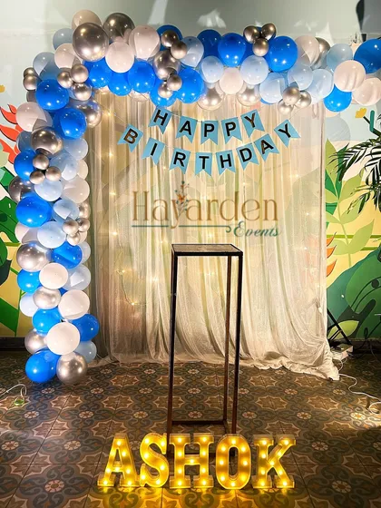 A classic blue, white, and silver balloon arch with a curtain backdrop and marquee letters. This is a versatile setup that works great for home parties.
