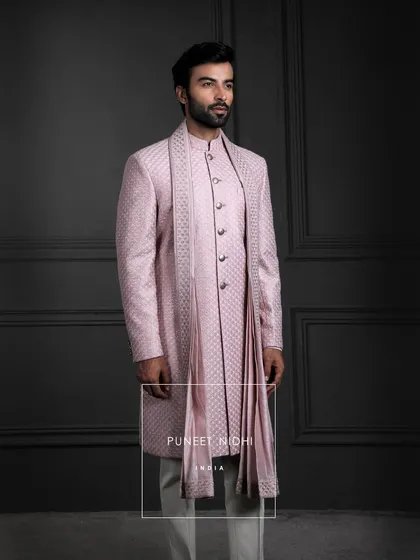 Soft as dawn, regal as legacy. This pink silk sherwani blooms with jacquard finesse, layered with a fish-scale achkan and stole, carrying tradition with graceful majesty.