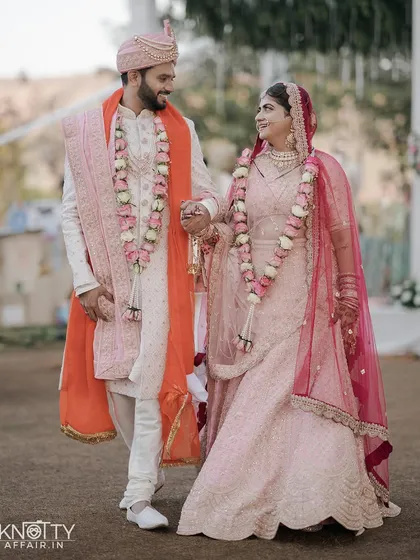 A joyful portrait of the newly married couple. Hand in hand, they walk together after their ceremony, sharing a look of love and happiness, their floral garlands adding a touch of tradition.