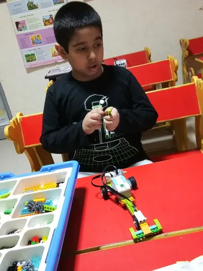 A student carefully assembles a robotic vehicle, focusing on the mechanical parts from his VEX kit.