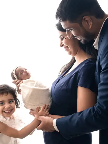 A happy family of four welcomes their newborn princess. The older sister's bright smile shows the joy of becoming a big sister in this classic, high-key portrait.