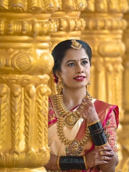 A classic portrait amidst golden pillars. Her makeup is timeless, with perfectly defined eyes and lips that complement her beautiful silk saree and temple jewelry.