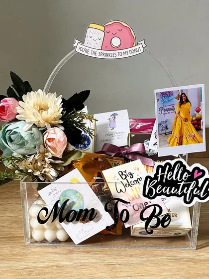 Celebrating a new chapter with a 'Mom to Be' hamper! This acrylic basket is filled with goodies like chocolates, skincare, and a bubble candle, all topped with a custom polaroid and cute decorations to pamper the new mommy.