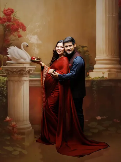 A full-length couple portrait set against a classical painted backdrop. The image highlights the couple's connection and the elegance of their traditional outfits.