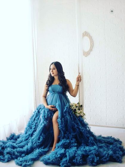 A stunning portrait of a mother-to-be in a deep blue gown, seated on a swing. This shot has a beautiful, almost painting-like quality.