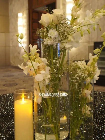 A classic and elegant centerpiece featuring white orchids and baby's breath in tall glass vases, paired with an LED candle for a timeless look.