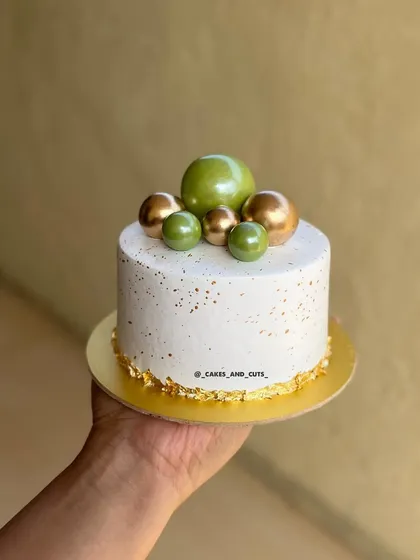 A simple and modern cake with green and gold spheres, gold leaf, and a speckled finish.