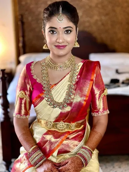 A bride looking radiant in a cream and red Kanchipuram saree. The custom pink blouse features unique puffed sleeves with detailed embroidery, adding a touch of personality to her muhurtham look.