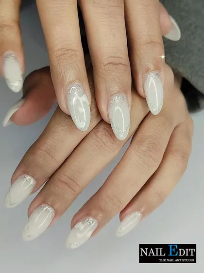 A dreamy and ethereal manicure with a milky white base and delicate silver glitter accents. The subtle sparkle and soft white marbling create a sophisticated and wintery feel.