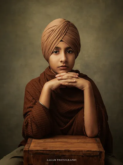 A soulful fine art portrait of a young boy in a turban. The painterly lighting and his poised expression create a powerful and timeless piece of art that captures his unique spirit.
