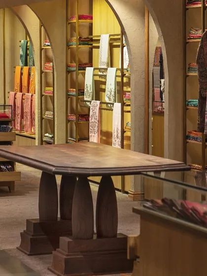 A custom-designed, heavy wooden table stands as a centerpiece in one of the upper-level lounges at Ahujasons. Its sculptural base and solid presence anchor the space, providing a surface for displaying and discussing heirloom-quality textiles.