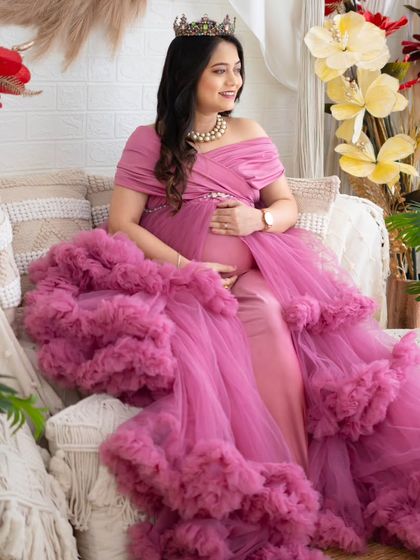 A regal portrait in a layered pink gown. The mom-to-be is seated on our studio couch, surrounded by lush plants and boho decor, looking like modern royalty.