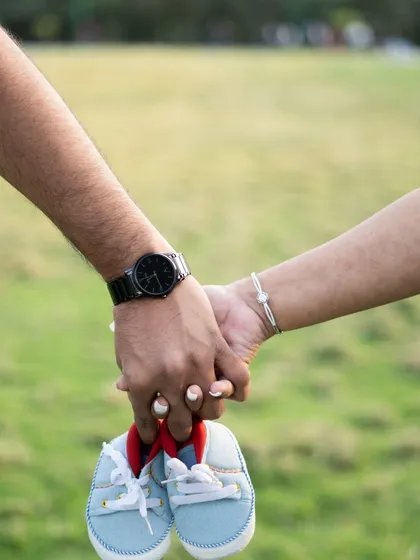 A close-up of a couple holding hands and a pair of baby shoes during their outdoor maternity session. A simple, sweet announcement.
