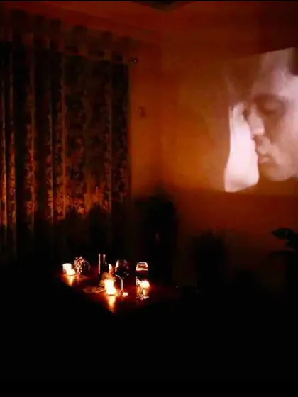 The room is dark and lit only by candles and the glow of a romantic movie scene, creating an intensely private atmosphere.