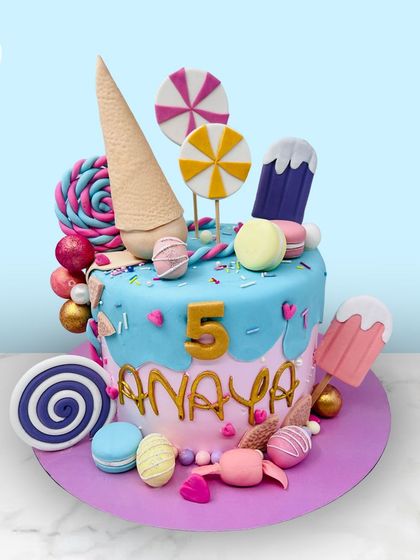 A candyland dream cake for Anaya's 5th birthday. This creation is overflowing with lollipops, ice cream cones, macarons, and other sweet treats.