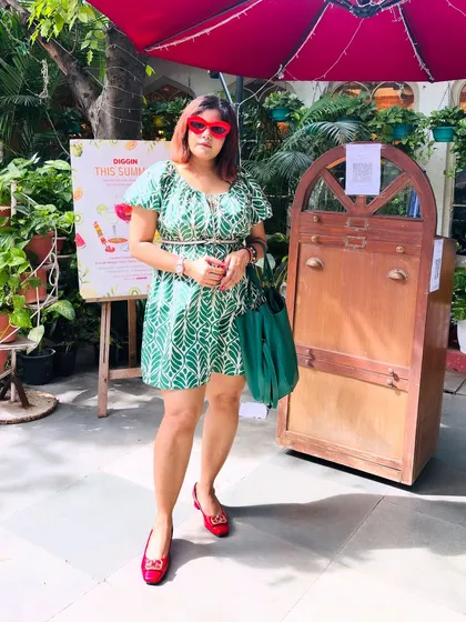 Posing in my green and red outfit in a sunny outdoor cafe setting.