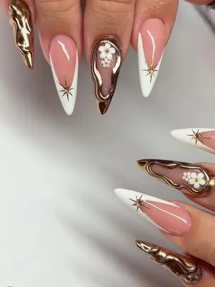 A high-fashion, artistic set of stiletto nails combining a white French tip with 3D gold chrome and floral details.