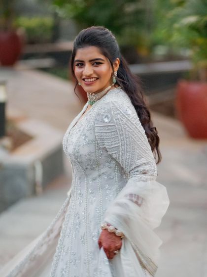 A happy, smiling portrait of the bride. Her hair is styled in a chic ponytail, which keeps the focus on the detailed neckline of her Sangeet jacket and her beautiful jewelry.